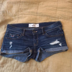  lågmidjade jeansshorts från Hollister - Snygga mörkblå jeansshorts från Hollister med slitna detaljer och upprullade benslut. Klassisk femficksmodell med logga på fickan och bakficka.  Midjemåttet är 38/39 i storlek 0/ w24 🩷priset är diskuterbart