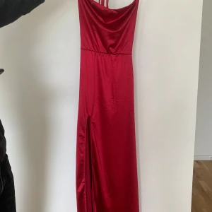 Röd långklänning med slits och snörning - Säljer min eleganta balklänning i satinliknande material som bara är använd en gång. Klänningen har smala axelband, en öppen rygg med justerbar snörning, hög slits framtill och en fantastisk röd färg som verkligen drar blickarna till sig.  Den sitter som en smäck och framhäver figuren på ett riktigt fint sätt. Storlek S och köpt från Shein.  Passar perfekt till balen, en fest eller något annat speciellt tillfälle. Skicka gärna ett meddelande om du är intresserad! OBS: fraktar inte!!!