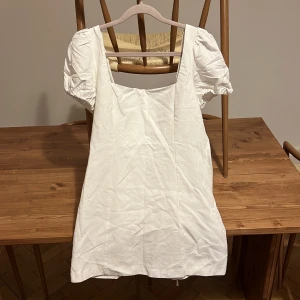 Vit kort klänning med puffärm och snörning - Superfin vit kort klänning med puffärmar, fyrkantig ringning och snygg snörning i ryggen. Klänningen har trasig dragkedja i sidan. Bonullstyg.