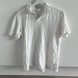 Vit pikétröja från NN07 - Klassisk vit pikétröja från NN07 med krage och korta ärmar. Tillverkad i bomull för en skön och luftig känsla. Perfekt för en clean och stilren look. Passar dig som gillar enkel och tidlös stil.