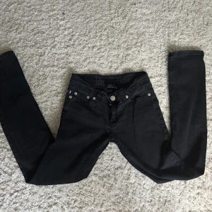 Svarta jeans Victoria Beckham - Svarta jeans från Victoria Beckham med snygga silverbroderade döskallar på bakfickorna. Jeansen har klassisk femficksdesign, silverfärgade knappar och är tillverkade i denim för en fin passform.