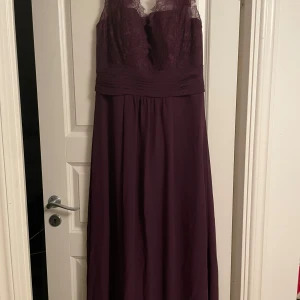 Mörklila långklänning med spets och snörning - Säljer en elegant mörklila balklänning med vacker spets upptill och plisserad midja. Klänningen har snörning i ryggen och en lätt v-ringad urringning. Perfekt för bal eller festliga tillfällen. Nypris:2499kr Mitt pris: 800kr eller bud + Frakt, aldrig använd❣️EU 40. Kontakta vid intresse ❤️
