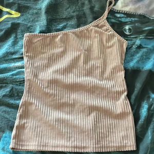 One shoulder topp - Säljer en beige ribbad one shoulder topp från SHEIN i storlek S. Toppen är tillverkad i ett mjukt, stretchigt material, säljer pågrund av att den ej kommer till användning