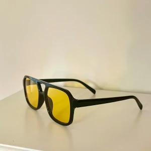 Snygga solglasögon med gula glas - Snygga solglasögon med svart ram och stora, fyrkantiga gula glas. Ramen är i plast och har en modern, oversized design som sticker ut😎Perfekta för dig som vill ha en cool accessoar med retrovibbar🤵🏼