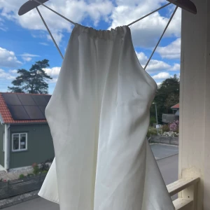 Vit halterneck linnetopp - Säljer en vit halterneck linnetopp med smala axelband och knytning i ryggen. Toppen har en luftig och lätt passform, perfekt för varma dagar.