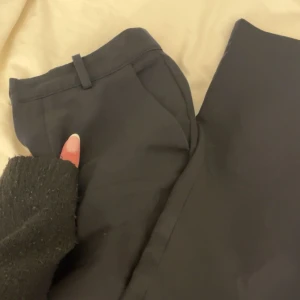 Svarta kostymbyxor från Bik Bok - Klassiska svarta kostymbyxor från Bik Bok med normal passform och hällor för bälte. Konstumbyxorna är highwaist. Byxorna har dragkedja och knapp framtill, perfekta till en stilren look. 