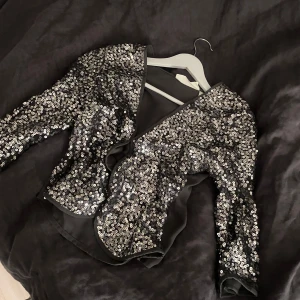 Silver paljettbolero - Säljer en glittrig silverfärgad paljettbolero från hm. koftan har trekvartsärm och är täckt av paljetter som ger en riktigt festlig look. Perfekt för dig som vill sticka ut och glänsa lite extra.