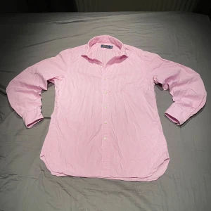 Rosa randig skjorta från Polo Ralph Lauren - Säljer en klassisk rosa och vit randig skjorta från Polo Ralph Lauren. Skjortan har lång ärm, knappar framtill och broderad logga på bröstet. Perfekt för dig som gillar stilrena plagg med snygga detaljer. Pris kan diskuteras