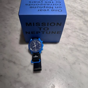 Omega x Swatch Mission to Neptune klocka - Säljer en Omega x Swatch Mission to Neptune från Bioceramic MoonSwatch Collection. Klockan har blå boett och blå urtavla med svarta detaljer samt svart textilband med Omega-logga.