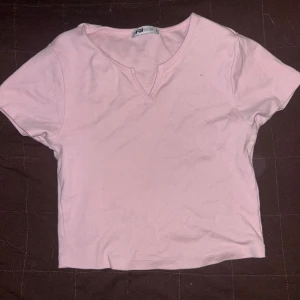 Ljusrosa croppad t-shirt från FB Sister - Säljer en ljusrosa croppad t-shirt från FB Sister. T-shirten har korta ärmar och en liten v-ringning vid halsen. Perfekt för dig som gillar en enkel och söt stil.