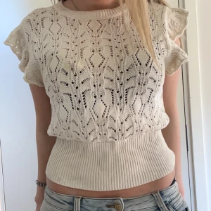 Vit stickad topp med spetsdetaljer - Säljer en söt vit stickad topp med korta ärmar och spetsliknande mönster. Toppen har bred ribbad midja och är croppad i modellen. 