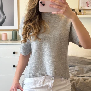 Ljusgrå stickad tröja - Säljer en ljusgrå stickad tröja med korta ärmar och rund hals. Tröjan har en enkel och stilren design, perfekt att matcha med jeans eller kjol. Mjuk och skön mot huden.