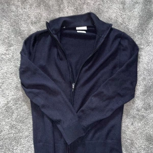 Mörkblå kofta med dragkedja - Säljer en stilren mörkblå kofta med dragkedja framtill. Tröjan har lång ärm, hög krage och ribbade muddar vid ärmslut och nederkant. Perfekt för lager-på-lager och enkel att matcha med olika outfits.