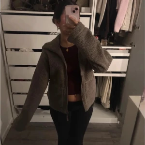Beige teddyjacka med dragkedja - Mysig beige teddyjacka med dragkedja framtill och stora fickor. Jackan har en hög krage och en avslappnad, oversized passform. Perfekt för kyliga dagar och enkel att matcha med olika outfits.
