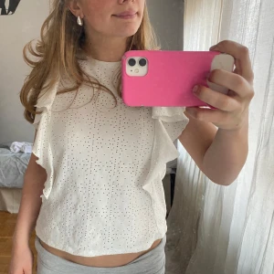 Vit blus med volang från Zara - Säljer en söt vit blus från Zara med små hålmönster och volangdetaljer längs axlarna. 