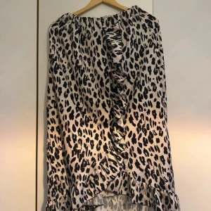 Leopardmönstrad kjol med volang - Säljer en snygg leopardmönstrad kjol med volangdetaljer framtill och längs fållen. Kjolen har lös passform och är perfekt för dig som vill sticka ut.