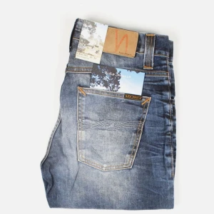 Blå jeansbyxor slimmade från Nudie Jeans - Säljer ett par helt nya klassiska blå jeans från Nudie Jeans med snygg slitning och kontrastsömmar. Byxorna har normal passform, raka ben och knappar i gylfen. Perfekta för dig som gillar en tidlös denimlook. Försmå för mig, Stolek 30:32