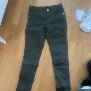 Mörkgröna slim byxor med guldknapp - Snygga mörkgröna byxor med slim passform och hög midja. Byxorna har guldknapp och dragkedja framtill samt fickor både fram och bak. Perfekta till vardags för en stilren look.