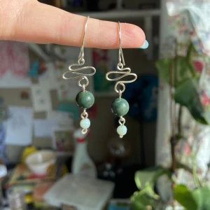Handgjorda örhängen med gröna stenar och silvertråd - Unika örhängen med konstnärligt böjd silverfärgad tråd och gröna pärlor i två nyanser. Hängande modell som ger ett bohemiskt och personligt uttryck. Perfekta för dig som vill sticka ut med ett handgjort smycke. Nickelfri 