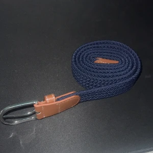 Mörkblått flätat bälte med bruna skinn-detaljer - Säljer ett mörkblått flätat bälte med snygga bruna skinn-detaljer och silverspänne. Bältet har en flexibel och stilren design som passar till många outfits. Perfekt accessoar för att lyfta din look.