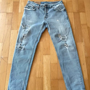 Ljusblå slitna jeans från DonDup - Ljusblå jeans med slitningar Dondups klassiska bakfickdesign. Femficksmodell med raka ben och knappgylf. Jeansen har en avslappnad look och är perfekta för en casual stil. Modell Brighton.            Priset är inte hugget i sten! 😊