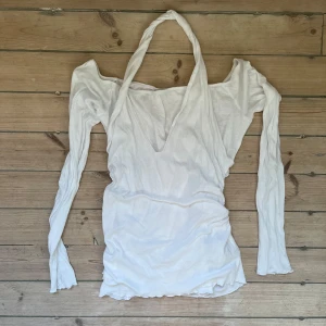 Vit långärmad topp med v-ringning från Zara - Säljer en vit långärmad topp från Zara med djup v-ringning och halterneck-detalj. Toppen är i mjukt material och har en unik design med öppna axlar. Perfekt för dig som vill sticka ut med en stilren look.