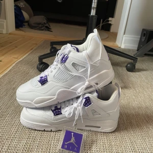 Nike Air Jordan 4 Retro 'Metallic Purple' - Säljer ett par fräscha Nike Air Jordan 4 Retro i vitt med lila detaljer. Skorna har klassisk meshpanel, snörning och den ikoniska Jumpman-loggan på plösen. Perfekta för dig som vill sticka ut med stilrena sneakers. Skriv för mer info eller frågor👌😀👍🏼priset är ej hugget i sten🤩