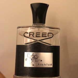 Creed Aventus Eau de Parfum 120ml - Lyxig parfym från Creed, Aventus, i en elegant flaska med svart och silverdetaljer. Flaskan rymmer 120 ml och har en distinkt svart kork med silveremblem på toppen. Doften är ikonisk och passar dig som vill sticka ut. Ca 95 % av perfymen kvar. Pris går att diskutera vid snabb affär.