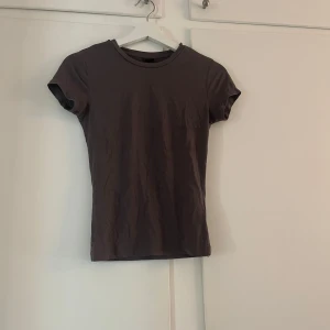 Brun t-shirt från Gina Tricot - En basic brun t-shirt från Gina Tricot med rund halsringning och korta ärmar. Perfekt att matcha med jeans eller kjol för en enkel och stilren look.