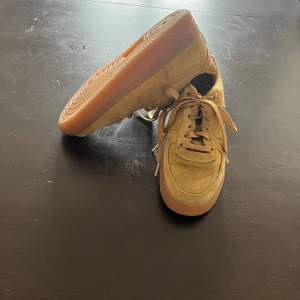 Beige Nike Air Force sneakers i mocka - Säljer ett par beige Nike Air Force sneakers knappt använda fint skick, har en platt, gummisula i ljusbrun färg. Perfekta för dig som gillar stilrena sneakers.