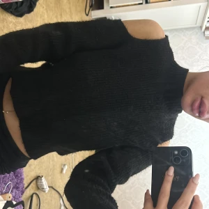 Svart stickad croppad tröja med cut out axlar - Säljer en svart stickad croppad tröja med cut out-detaljer vid axlarna. Tröjan har lång ärm.