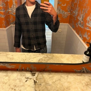 Flanellskjorta, Uniqlo - Säljer en svart och grå rutig skjorta från Uniqlo. Skjortan har en avslappnad passform och är perfekt att bära över en t-shirt. Säljer för den är för liten för mig. Passar perfekt för någon med M!!