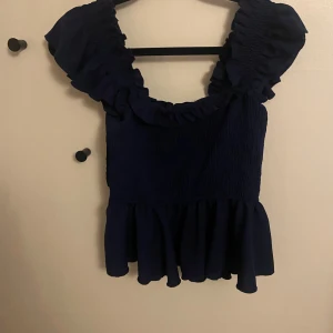 Mörkblå volangtopp  - Säljer en mörkblå topp med volang nertill och axelpartier med rynkande material i mitten av toppen. Toppen har en croppad passform och är tillverkad i ett stretchigt material med struktur. 💕💕