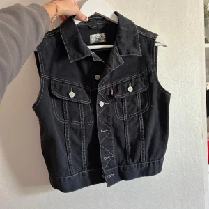 Svart jeansväst med vita sömmar - Säljer denna fina jeansvästen i storlek M. Använd ett fåtal gånger🥰