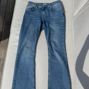 Blå bootcut jeans från Gina tricot - Säljer ett par klassiska blå bootcut jeans från Gina tricot storlek 40. Jeansen har normal passform, fem fickor och dragkedja med knapp. Stretchigt material och medelhög midja. Bra skick förutom lite slitage på byxkanten vid fötterna