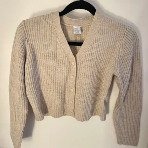 Beige ribbad kofta från Lindex - Säljer en beige ribbad kofta från Lindex i storlek 134/140. Koftan har långa ärmar och knappar framtill!