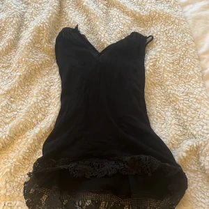 Svart kortklänning med spets från Eya Collition - Supersöt svart lång blus från Eya Collition med smala axelband och v-ringning. Klänningen har fina spetsdetaljer nertill och en lätt, luftig känsla. Perfekt för dig som gilla en enkel men ändå elegant stil. Köpt i Grekland minns inte för hur mycket 