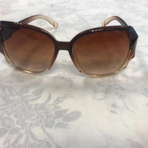 Bruna oversized solglasögon med metall-detalj - Stora solglasögon med bruna tonade glas och bågar i brun plast som övergår i beige. Snygg metall-detalj vid skalmarna. Perfekt accessoar för en trendig look.