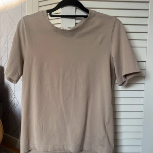 Beige t-shirt från Gina Tricot - En enkel och stilren beige t-shirt från Gina Tricot, basically basics-kollektionen. T-shirten har rund halsringning och korta ärmar. Perfekt att matcha med jeans eller kjol för en clean look.
