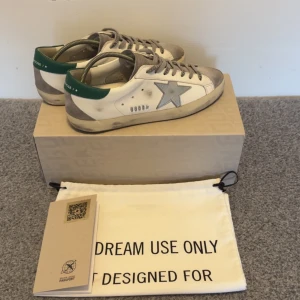 Golden Goose Superstar sneakers - Golden Goose Superstar sneakers med en grön detalj i storlek 40. Mycket bra skick, anvendt extremt sparsamt. Kvitto dustbag box och certifiering kortet ifrån Golden goose. Om du har några funderingar hör av dig 👍