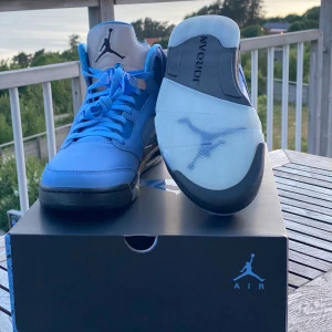 Nike Air Jordan 5 UNC Retro- OANVÄNDA  - Säljer ett par helt oanvända Nike Air Jordan 5 UNC i ljusblå mocka med svarta och vita/silver detaljer. Klassisk snörning, genomskinlig sula och ikoniska Jumpman-loggan. Kommer i originalförpackning – aldrig provade, helt nya. Exklusiv modell – Nypris: 5125 kr. Mitt pris: 3200 kr  📦 Skickas spårbart eller möts upp. 💬 Pris kan diskuteras vid snabb affär. Perfekta för dig som gillar sneakers med unik färg, stil och premiu