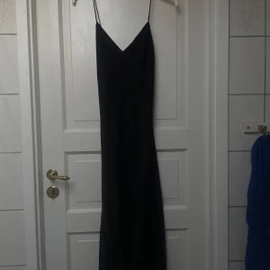 Svart långklänning med smala axelband från ASOS DESIGN - Säljer en svart långklänning från ASOS DESIGN med smala axelband och v-ringad hals. Klänningen har en elegant och enkel design som faller snyggt längs kroppen. Perfekt för dig som gillar minimalistisk stil.