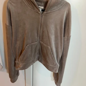 Beige hoodie i velour från H&M - Mysig beige hoodie i mjuk velour från H&M. Tröjan har dragkedja framtill, två fickor och huva. Perfekt för en avslappnad stil och sköna dagar.