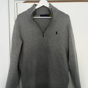 Stickad quarter-zip Polo Ralph Lauren - Snygg grå stickad  från Polo Ralph Lauren med halv dragkedja och broderad logga på bröstet. Tröjan har hög krage och ribbade muddar vid ärmslut och nederkant. Perfekt för lager-på-lager-stil. Köptes ny för ~2300kr