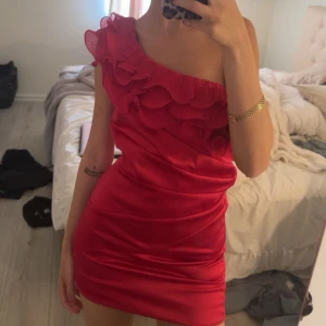 Röd one shoulder klänning med volang - Säljer en snygg röd kortklänning i satin med one shoulder-design och stora volangdetaljer längs axeln och överdelen. Klänningen har en figurnära passform och är perfekt för festliga tillfällen. Köpt på vinted , stor ingen storlek men skulle säga att de är en s-xs jag är en xxs och den är lite pösig 