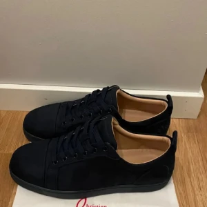 Mörkblå  sneakers från Christian Louboutin - Säljer ett par mörkblå sneakers från Christian Louboutin i mocka med klassisk röd sula. Skorna har rund tå, mörkblå snören och diskreta detaljer. Insidan är beige och de har en stilren look som passar till mycket.