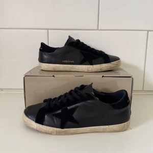 Golden goose - Svarta sneakers från Golden Goose med ikonisk svart stjärna på sidan. Skorna har snörning, rund tå och en vit, något smutsad sula för den klassiska worn looken. Tillverkade i skinn och mocka med detaljer i svart och diskret guldtext på sidan. I mycket bra skit, kvitto finns även 