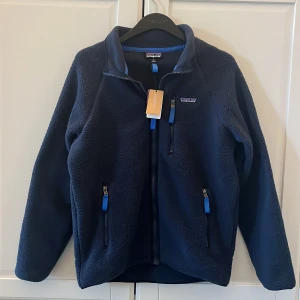 Mörkblå fleecejacka från Patagonia - Mörkblå fleecejacka från Patagonia. Storleken är S och jag skulle säga att längden sitter som S men bredden är lite mer åt M. Perfekt nu för lite kallare sommardagar/kvällar! Hör av dig vid frågor!😁