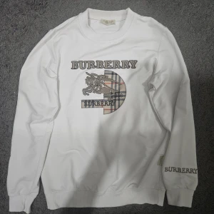 Burberry sweatshirt - Stilren Burberry sweatshirt - Vit, storlek (S)  Snygg och bekväm vit sweatshirt från Burberry med klassisk logga och det ikoniska mönstret i mitten. Tröjan har detaljerad brodyr på bröstet och ärmen, vilket ger ett lyxigt intryck. Perfekt för dig som vill kombinera stil med komfort.