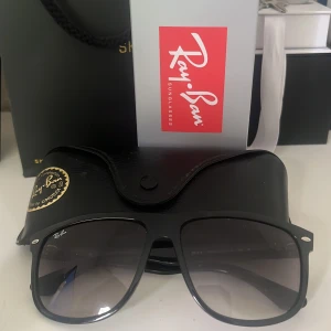 Svarta Ray-Ban solglasögon - Stilrena svarta Ray-Ban solglasögon med breda bågar och mörktonade glas. Klassisk fyrkantig form och diskret Ray-Ban-logga på linsen. Kommer med originalfodral och etikett. Perfekta för dig som vill ha en tidlös och cool look. Pris kan diskuteras!